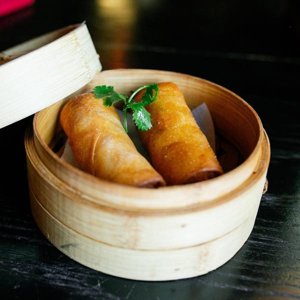 Two crispy Old Thousand spring rolls with cilantro in a bamboo steamer basket.