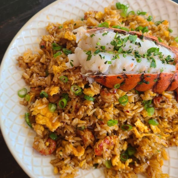 Old Thousand's lobster fried rice, garnished with green onions and parsley, on a white plate.