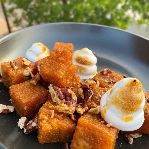 Sweet potato cubes with toasted marshmallows and pecans on a dark plate.