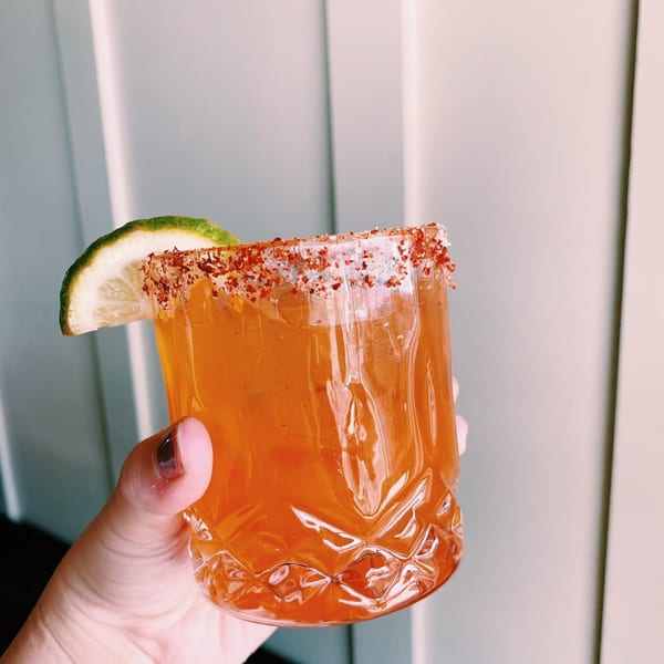 A hand holds an Old Thousand cocktail with a chili-salt rim and lime wedge.